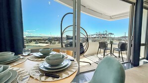 Un comedor con vistas al puerto y grúas, con una mesa redonda, platos y cubiertos.