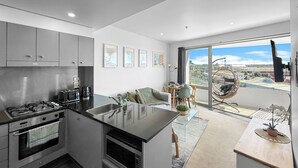 Una cocina moderna con una isla central, un área de comedor con una silla colgante y un amplio ventanal con vistas a la ciudad.