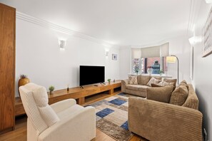 A modern living room with a flat-screen TV, a wooden coffee table, a beige sofa, and a patterned rug.