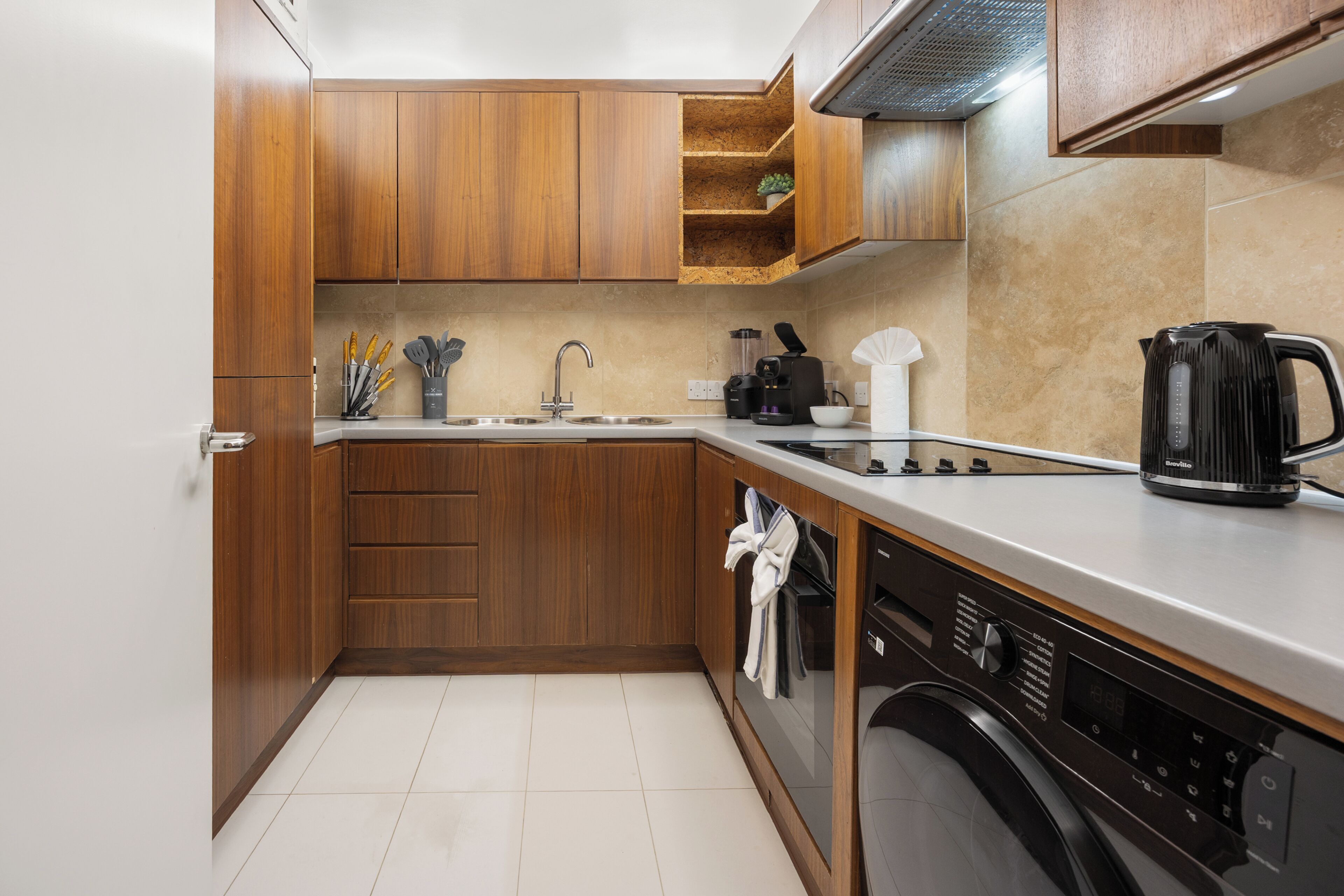 A compact kitchen with wooden cabinets, a stainless steel sink, a coffee maker, and a dishwasher.