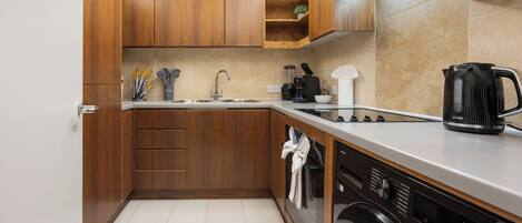 A compact kitchen with wooden cabinets, a stainless steel sink, a coffee maker, and a dishwasher.