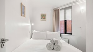 Ein Hotelzimmer mit Bett, Kissen, einem Fenster mit Vorhängen, einem Heizkörper und einer Tür mit Schloss.