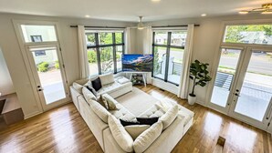 Ein geräumiges Wohnzimmer mit einer großen, winkelförmigen Couchgarnitur, einem Flachbildfernseher und großen Fenstern, die einen Blick ins Freie bieten.