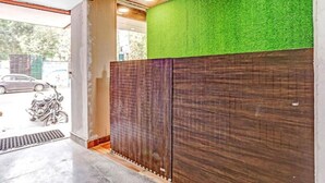 A reception area with a green artificial grass wall, wooden paneling, and a motorcycle parked outside. - Hotel Jeet Stay  (New Delhi)