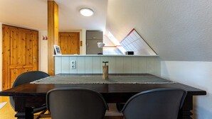 Une cuisine moderne avec une table à manger en bois, des chaises noires et un petit îlot central surmonté d’une lampe blanche.