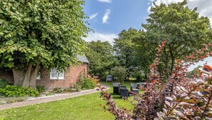 Un bâtiment en briques avec un grand arbre devant, un chemin pavé et du mobilier d’extérieur.