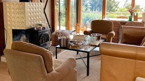 A cozy room with a fireplace, comfortable seating, and large windows offering a view of the outdoors. - Captain John's Hideaway (Stinson Beach)