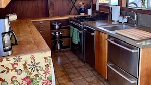 A kitchen with wooden cabinets, a gas stove, stainless steel appliances, and a tiled floor. - Captain John's Hideaway (Stinson Beach)