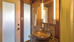 A bathroom with a wooden vanity, a large mirror, and a bowl sink. - Captain John's Hideaway (Stinson Beach)