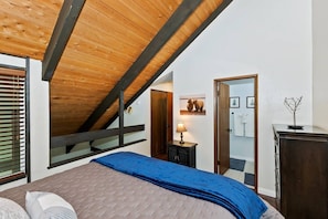 Ein Schlafzimmer mit schrägen Wänden, einem Bett mit blauer Decke, einer Holzkommode und einem Spiegel.
