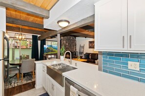 A modern kitchen with a stone accent wall, a built-in sink, and a dining area with a view. - Retreat at Snow Summit: By Destination Big Bear: Walking Distance to Snow Summit! Close to the Village! (Big Bear Lake)