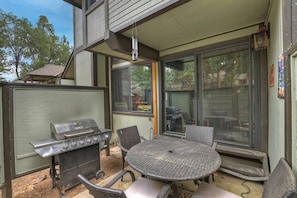 Une terrasse extérieure équipée d’un barbecue, de chaises en osier et d’une porte vitrée donnant accès à un espace protégé par des moustiquaires.