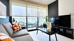 A modern living room with a sofa, a coffee table, a TV, and a balcony with a city view.