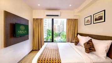 Habitación de hotel con cama, televisor montado, ventana con cortinas e imágenes enmarcadas en la pared.