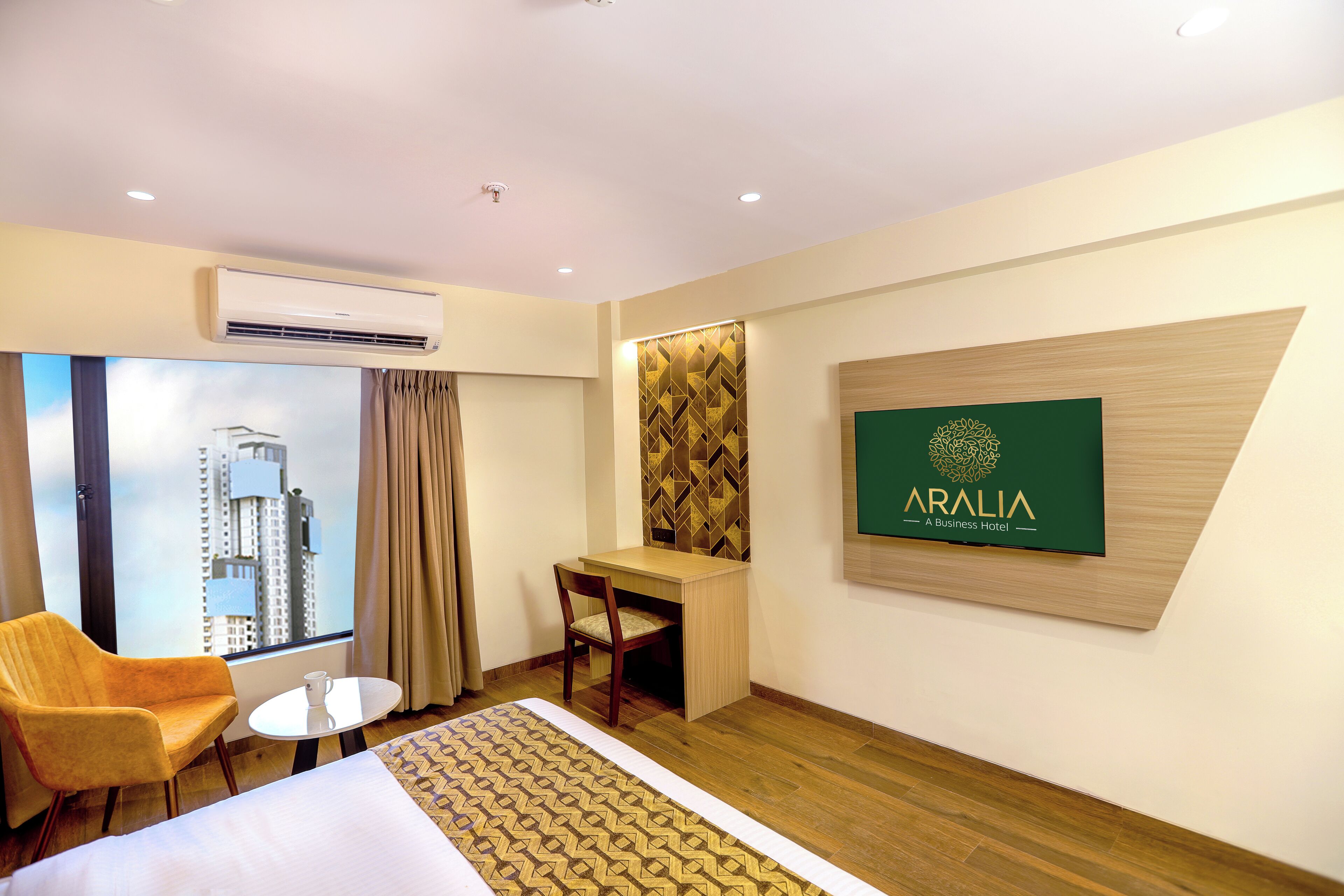 A hotel room with a bed, a desk, a chair, a small table, and a large window with a view of a building.