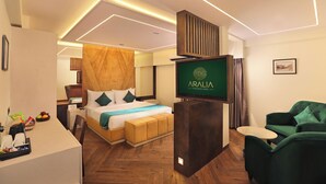 A modern hotel room with a bed, a desk, a green armchair, and a TV displaying the hotel name. - Aralia International Airport Mumbai (Mumbai)