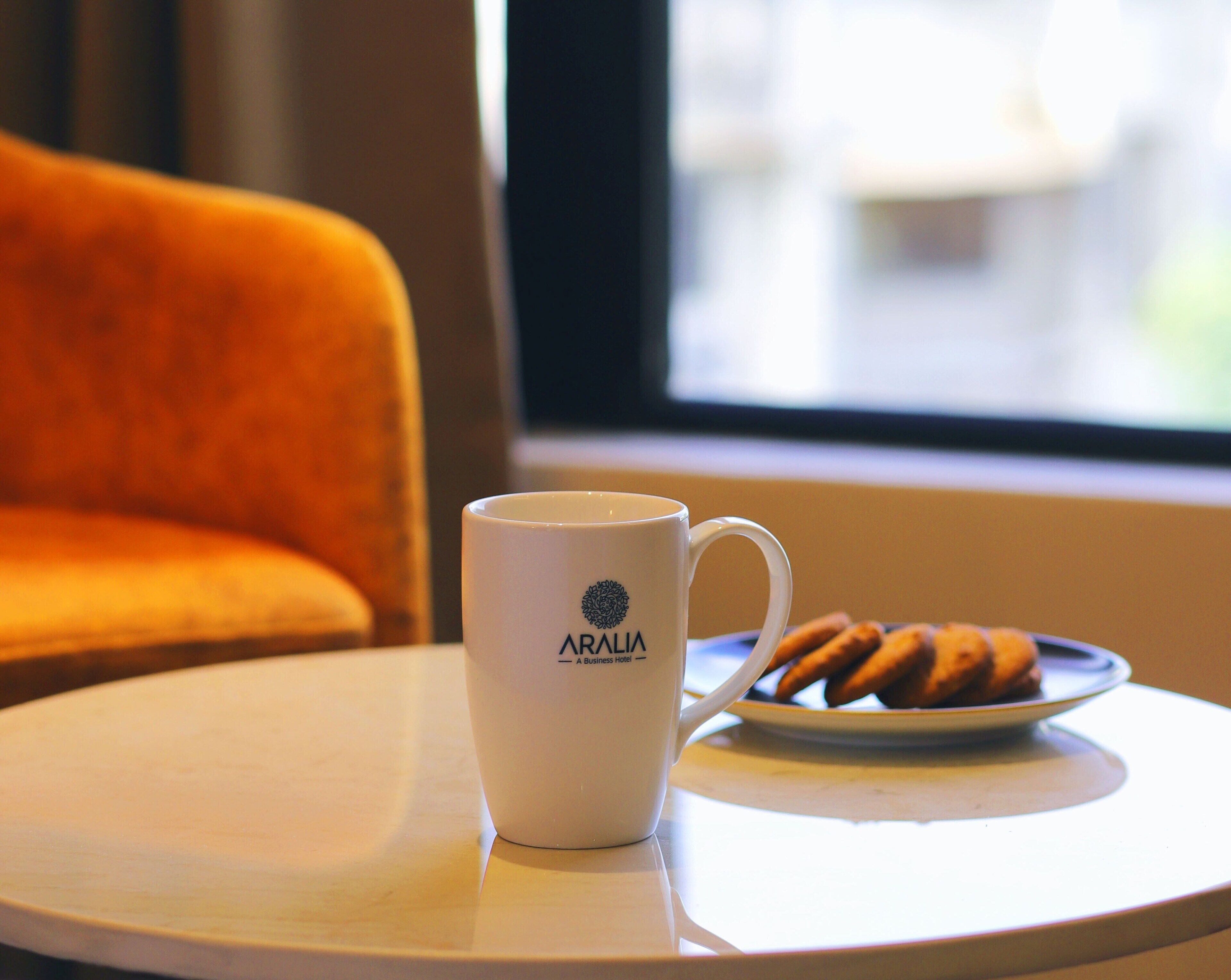 Une tasse blanche ornée du logo « ARALIA, hôtel d’affaires », posée sur une table ronde.