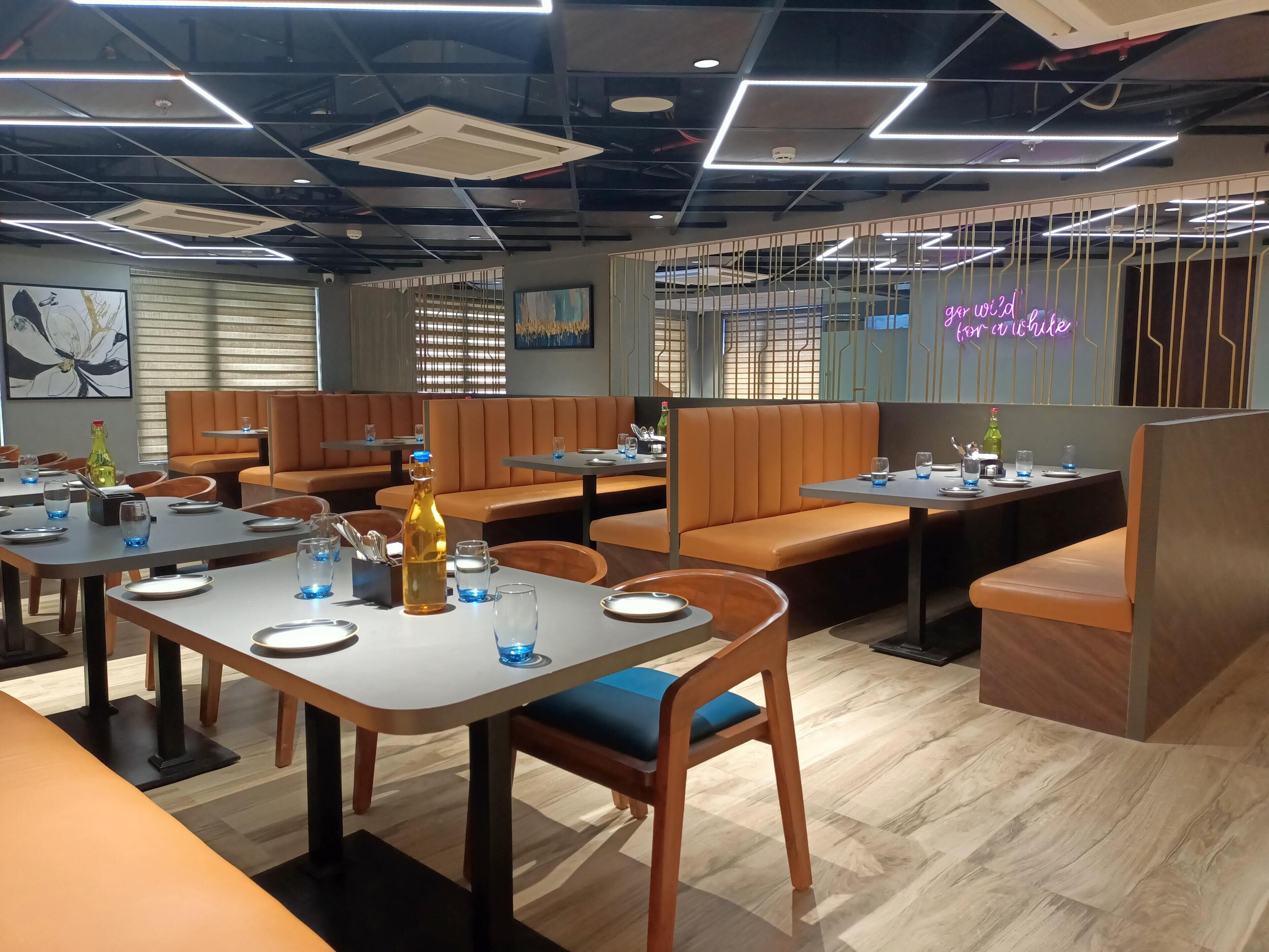 Ein modernes Restaurant mit Sitzgelegenheiten in Form von Boxen und Tischen, einige davon mit blauen Gläsern und Flaschen.