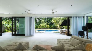 Un salon moderne doté d’un grand canapé, d’une piscine et offrant une vue sur une végétation luxuriante.