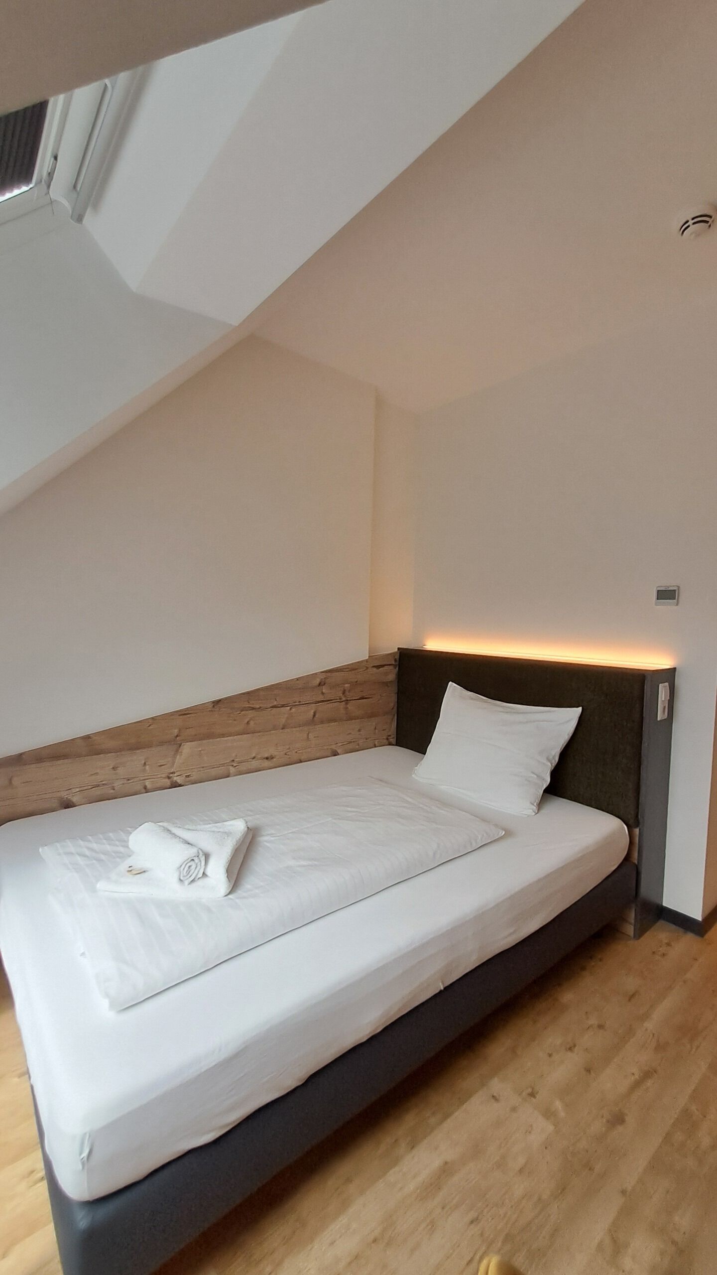 A single bed with a wooden headboard, a white mattress, and a neatly folded towel.