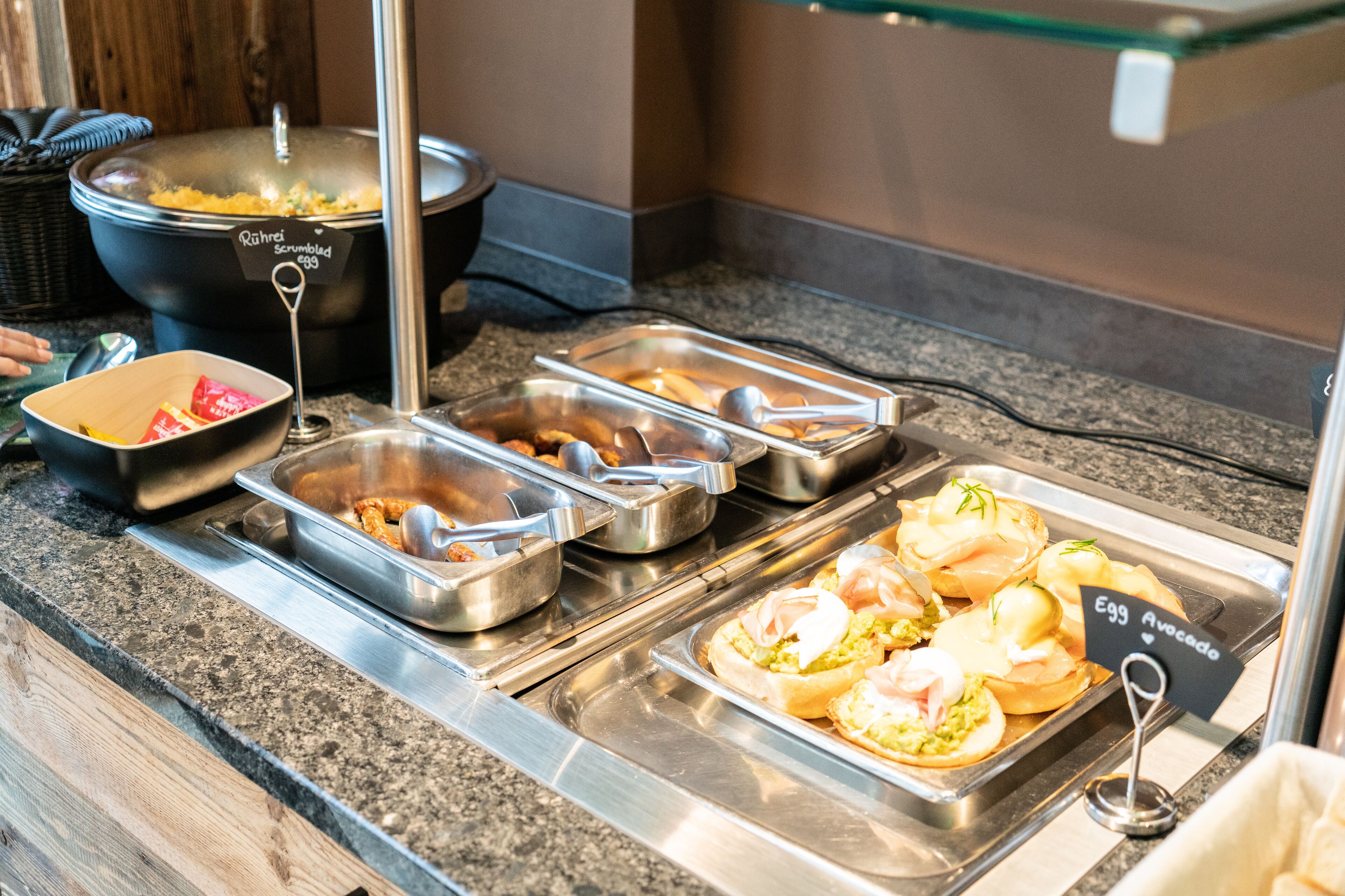 Un bufé con diversas opciones de comida, incluyendo huevos revueltos, aguacates y otros platos.