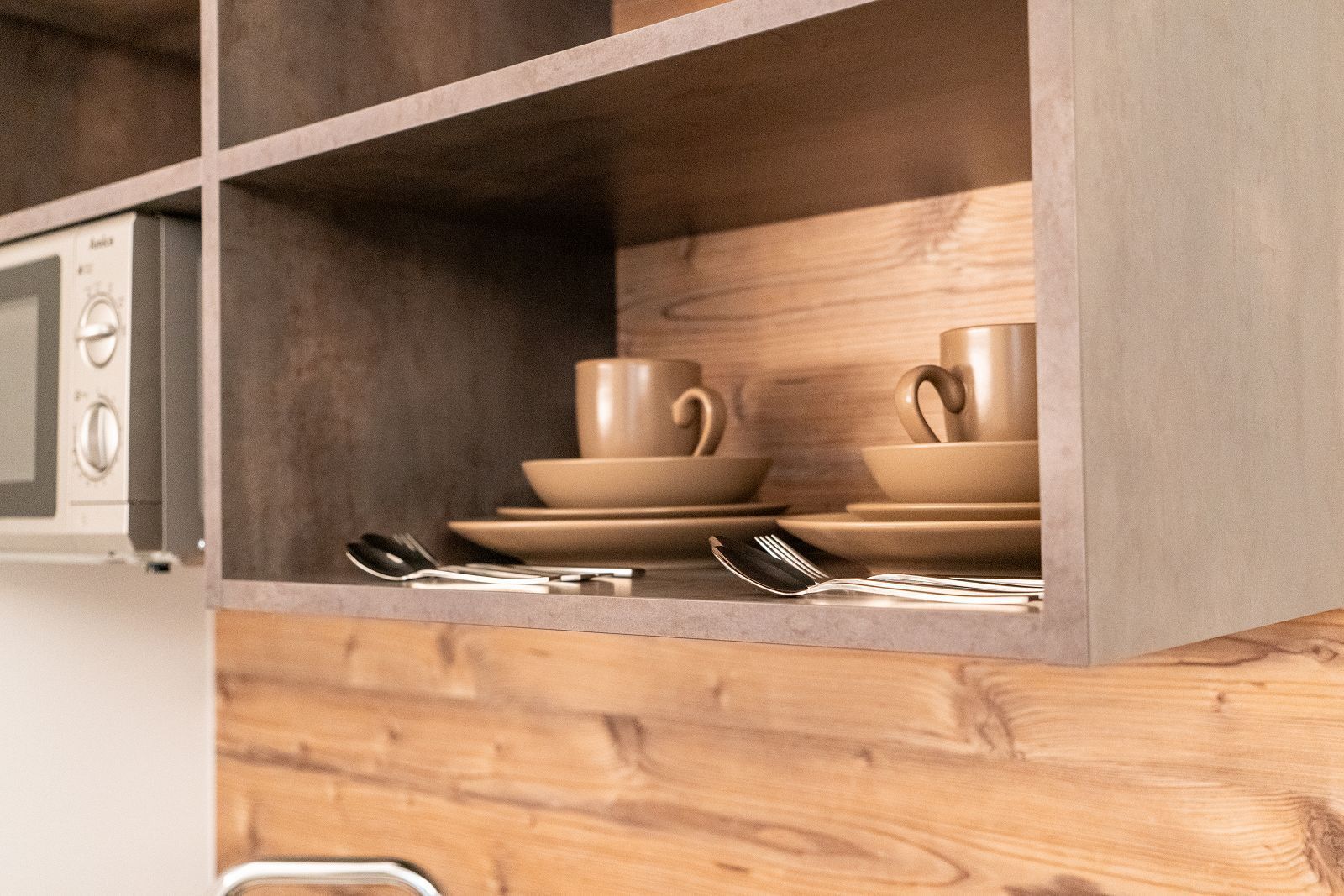 A kitchen with wooden cabinets, a microwave, and stacked beige dishes.
