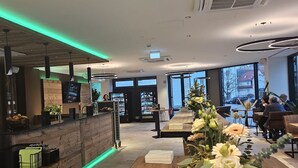 Een modern interieur met een houten receptiebalie, een verlichte balie met groene tinten, en een groot raam met uitzicht op buiten.