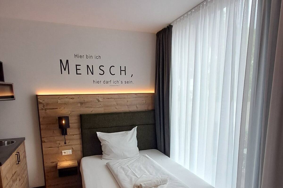 Een moderne hotelkamer met een houten hoofdeinde, een bed met witte lakens, een nachtkastje met een lamp en een wandbord.