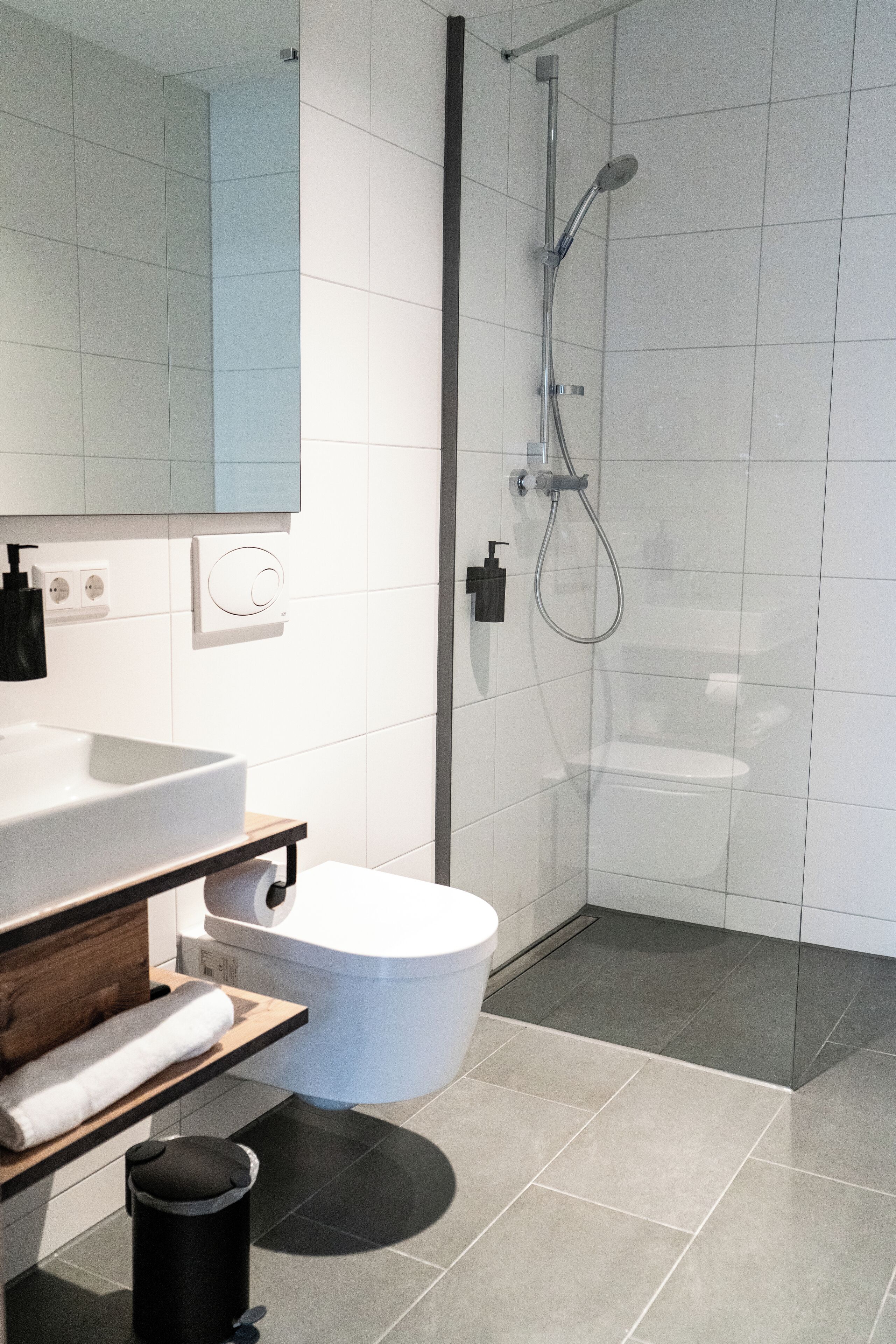 Un baño moderno con ducha de vidrio, lavamanos blanco y un inodoro.