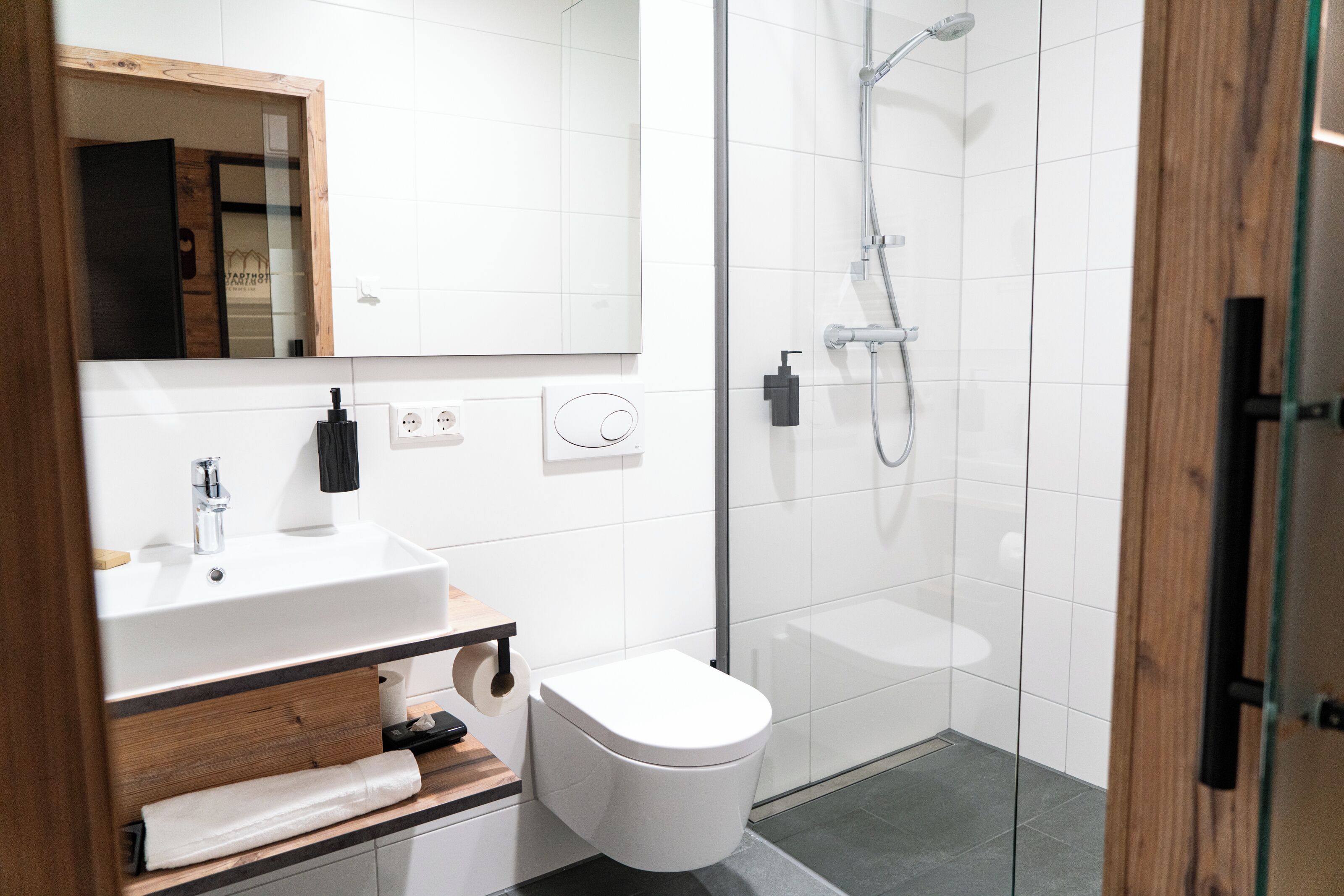 A modern bathroom with a white sink, mirror, toilet, and glass shower enclosure.