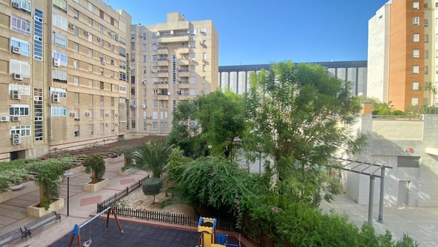 A residential building with multiple balconies, a playground, and a small garden area. - Rentalsevilla en Nervión (Sevilla)
