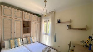 A bedroom with two beds, a desk, and a chair. There are built-in wardrobes and a shelf with books. - Rentalsevilla en Nervión (Sevilla)