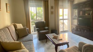 A living room with a sofa, armchair, coffee table, and a cabinet with a television. - Rentalsevilla en Nervión (Sevilla)