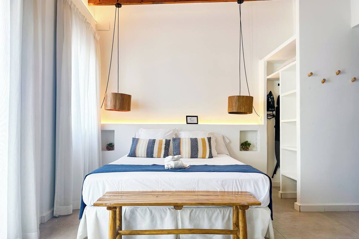Un dormitorio con cama, mesitas de noche, un banco de madera y una lámpara colgante.