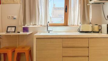 Una cocina con ventana, un fregadero, microondas, tostadora y dos taburetes.