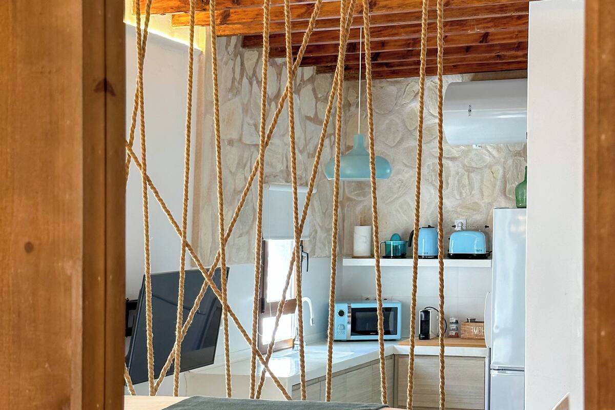 Un dormitorio con una cama, techo de madera y una zona de cocina al fondo.