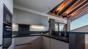A modern kitchen with grey cabinets, a black countertop, and a wooden ceiling.