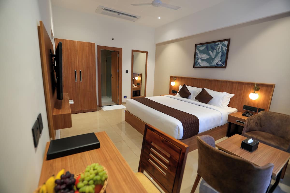 A hotel room with a bed, bedside table, chair, desk, and a fruit bowl.