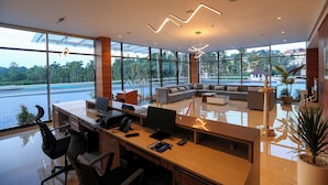 A modern office with a large desk area, comfortable seating, and large windows overlooking a scenic view. - Hotel Saffron Wayanad (Sulthan Bathery)