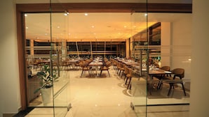 A spacious restaurant with multiple dining tables and chairs, a modern interior design, and a view through glass doors. - Hotel Saffron Wayanad (Sulthan Bathery)
