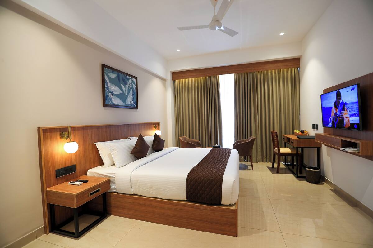 A hotel room with a large bed, a desk with a chair, a television, and a ceiling fan.