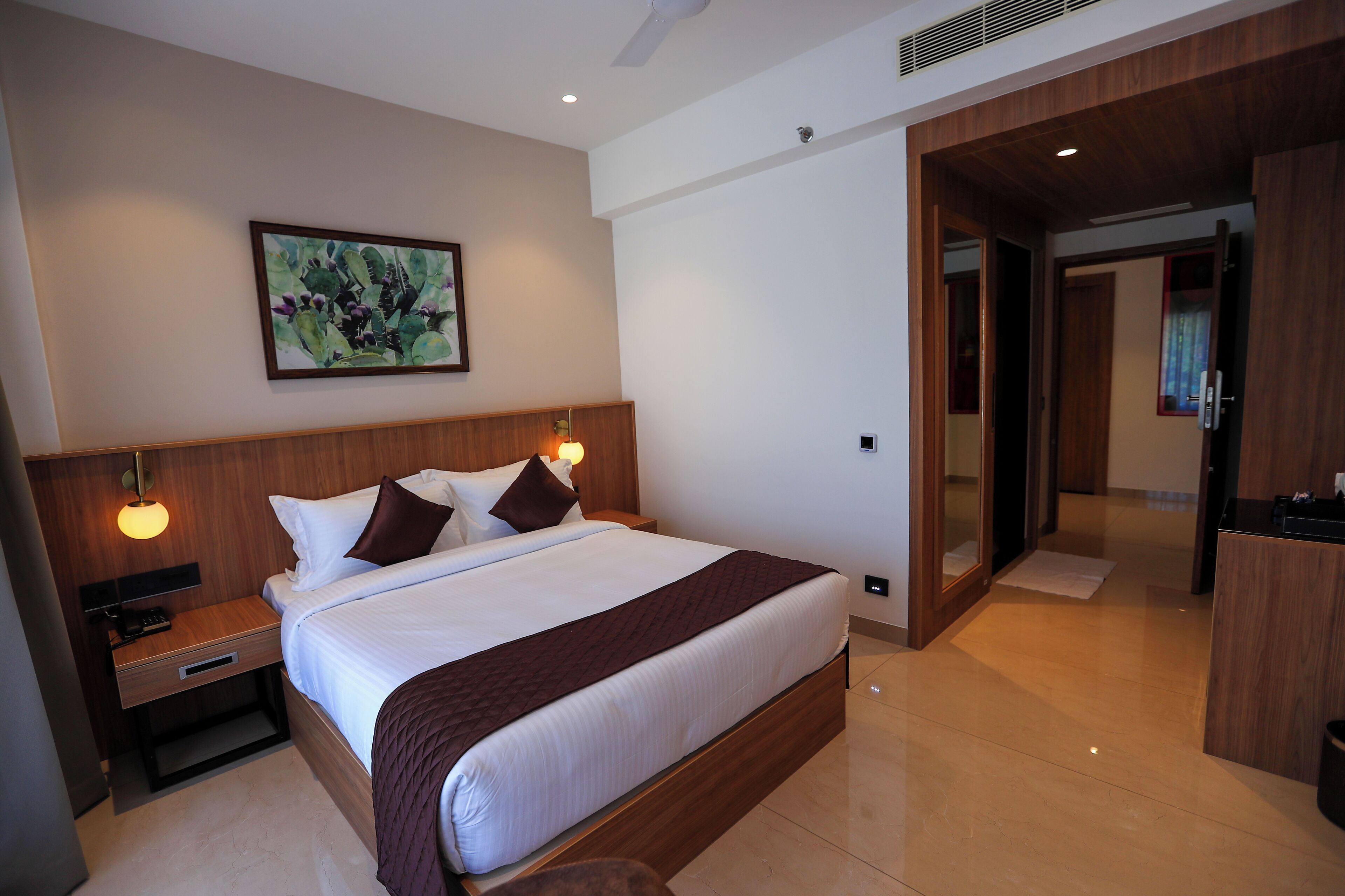Una camera d'albergo moderna con un letto grande, una testiera in legno, lampade sui comodini e un quadro appeso al muro.