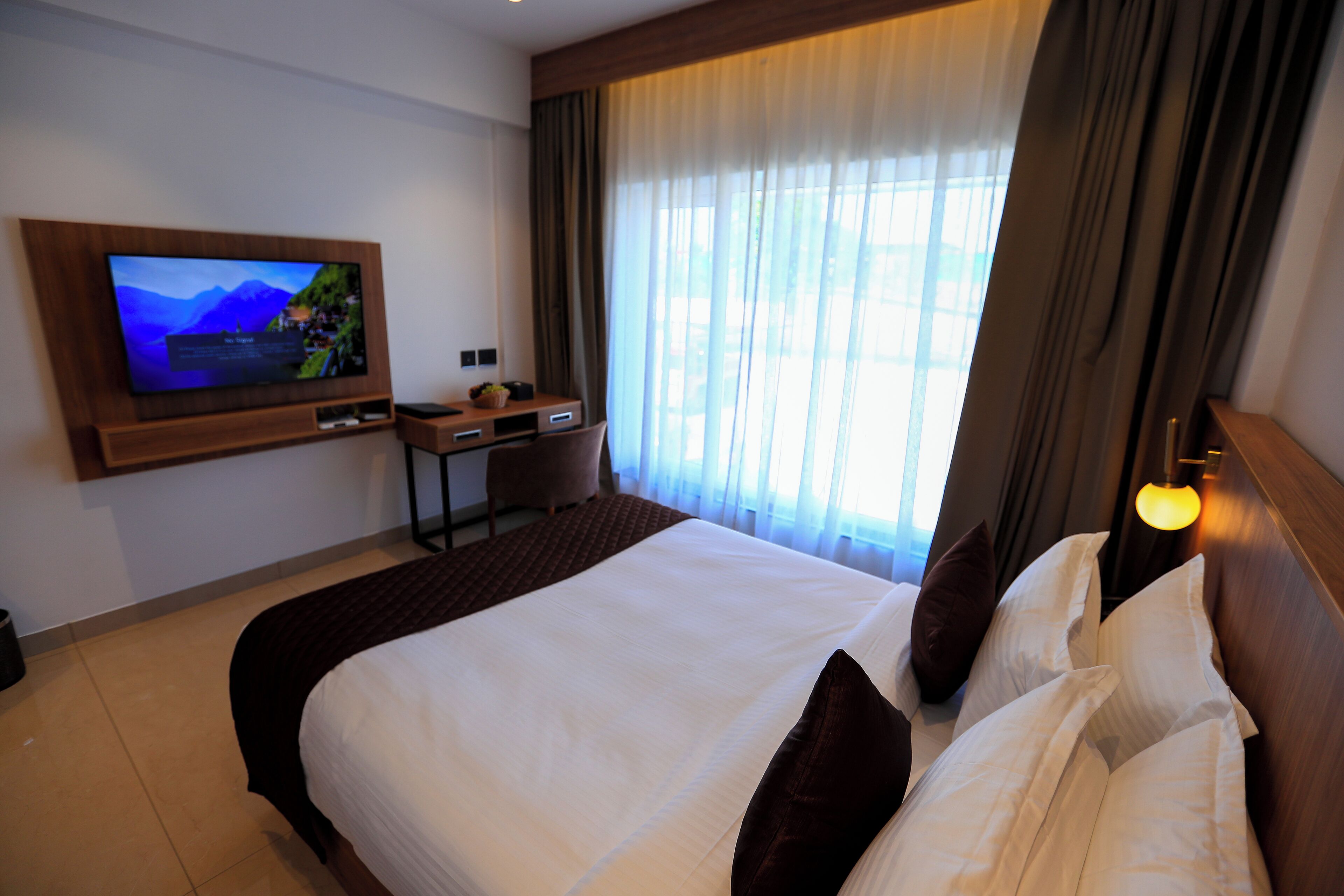 Une chambre d’hôtel avec un grand lit, un téléviseur fixé au mur, un bureau et une fenêtre avec des rideaux.