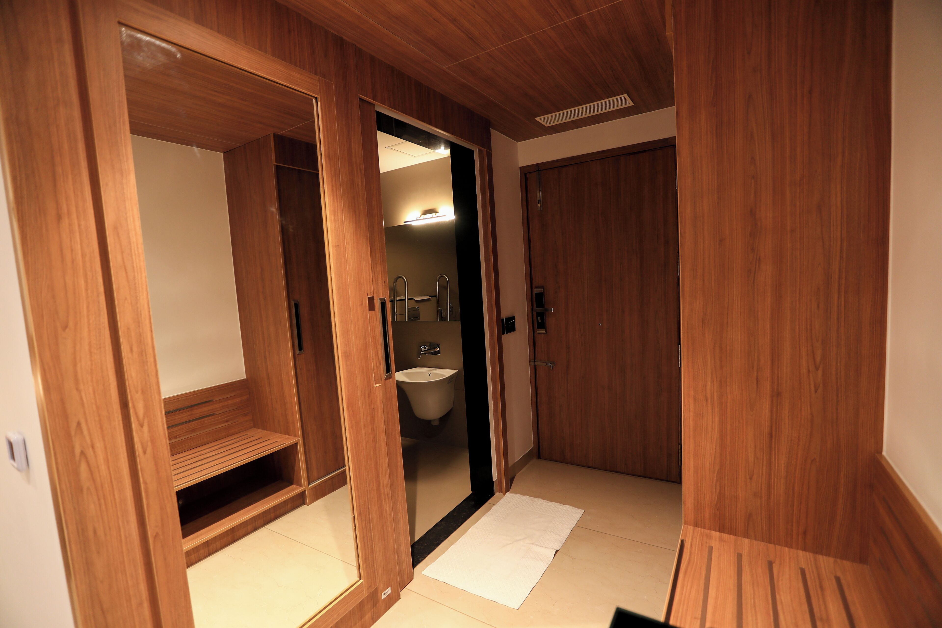 A wooden walk-in closet with a mirror, a sink, and a door leading to another room.