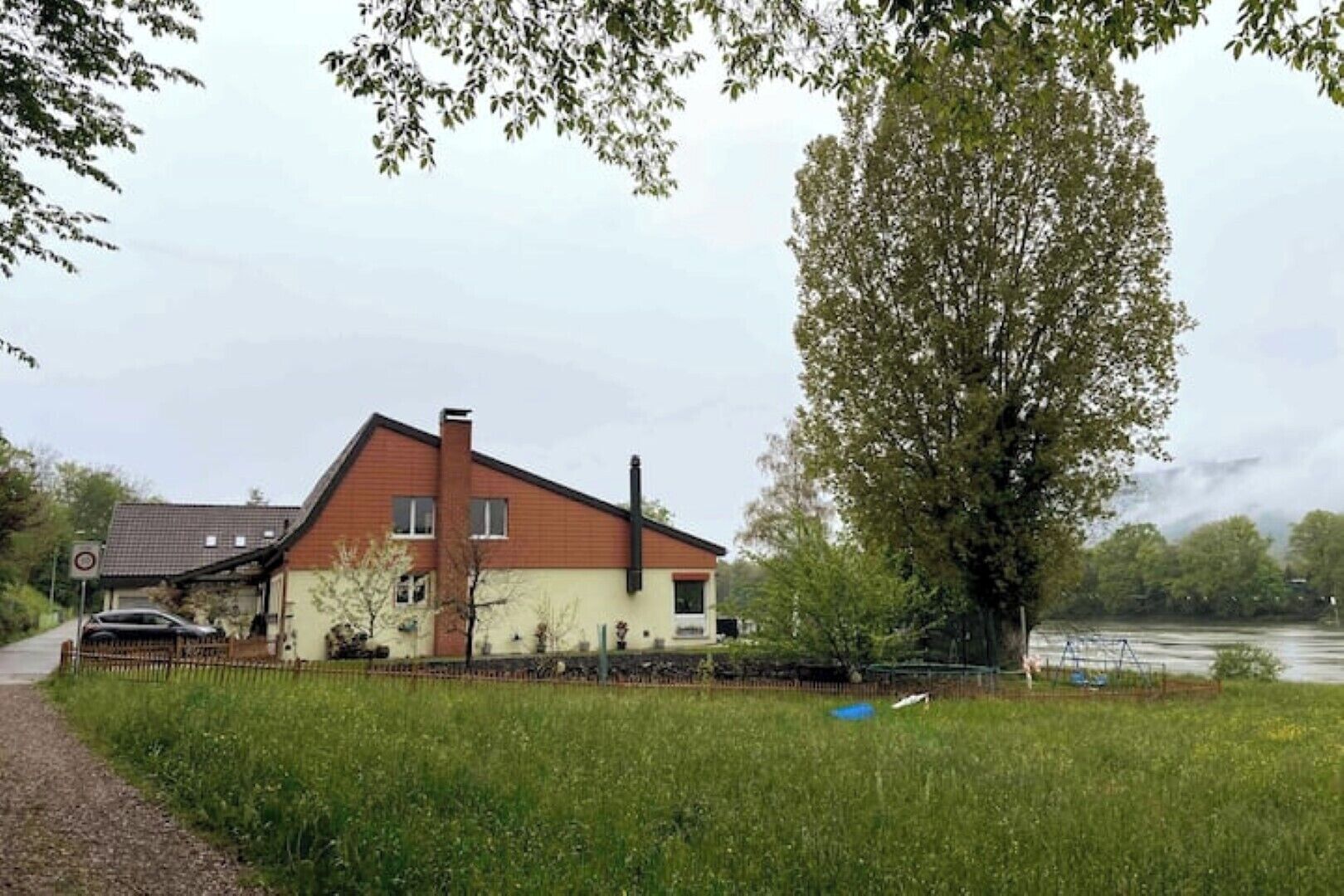 Ein zweistöckiges Haus mit geneigtem Dach, einem Schornstein und einem umzäunten Garten.