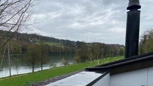 Blick aus einem Fenster auf einen Fluss, mit einer grünen Wiese und Bäumen im Hintergrund.