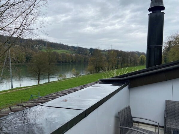 Une vue depuis une fenêtre donnant sur une rivière, avec une zone herbeuse et des arbres en arrière-plan.