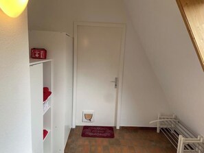 Un petit couloir étroit avec une porte blanche, un radiateur blanc et un tapis rouge sur le sol.