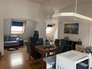 Ett modernt vardagsrum med en matplats, en tv och en kristallkrona.