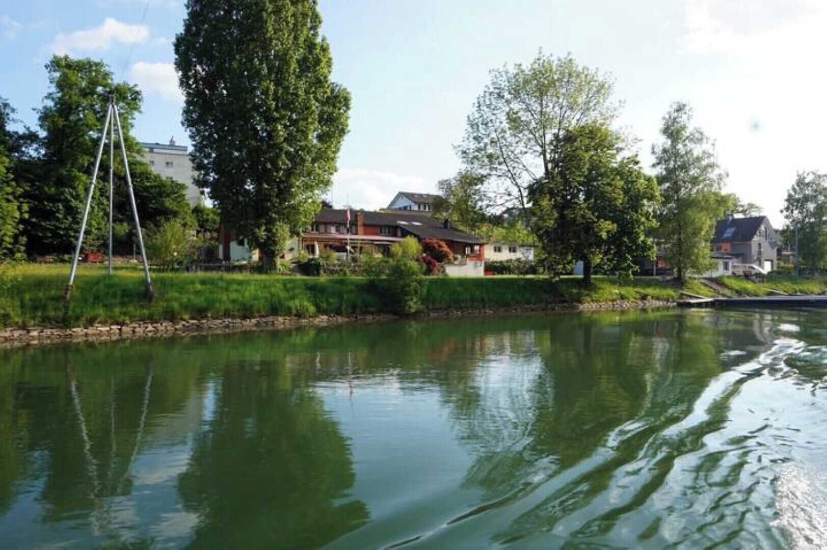 Un río tranquilo con una casa y árboles al fondo.